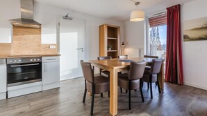 A modern kitchen with a built-in oven, a wooden dining table with chairs, and a view through a window with curtains. - Winterberg Stay with Beautiful View (Winterberg)