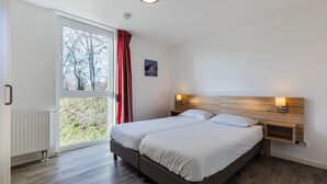 A bedroom with a large window, a radiator, a wooden headboard, and a bedside table with a lamp. - Winterberg Stay with Beautiful View (Winterberg)