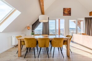 A dining area with a table, chairs, a pendant light, and a city view through large windows.
