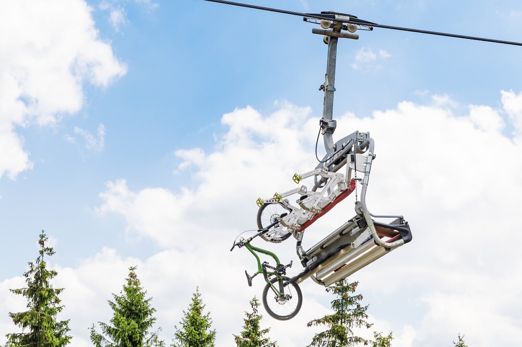 Una bicicleta colgando de un cable, con cielo despejado y árboles al fondo.