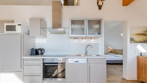 A modern kitchen with a built-in oven, microwave, and dishwasher, a wooden floor, and a view of a bedroom with a bed and a nightstand. - Spacious, modern apartment, near center (Winterberg)
