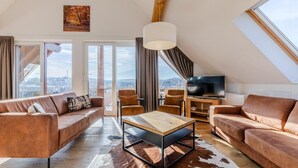 A modern loft apartment with a large window, a flat-screen TV, leather sofas, and a wooden coffee table. - Spacious, modern apartment, near center (Winterberg)