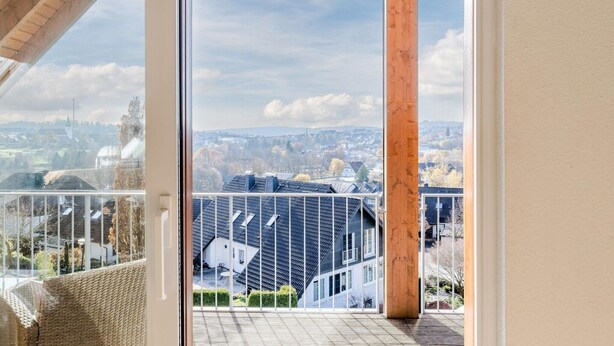 A balcony with a view of a cityscape, a wooden column, and a white railing. - Spacious, modern apartment, near center (Winterberg)