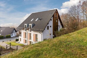 Ein modernes Haus mit geneigtem Dach, großen Fenstern und einem kleinen Balkon.