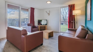 Una sala de estar moderna con sofá, sillón, televisor y lámpara.