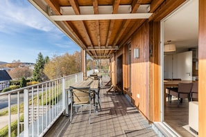 Eine Holzterrasse mit Sitzgelegenheiten und Blick auf die Umgebung, sowie ein Gebäudeeingang.