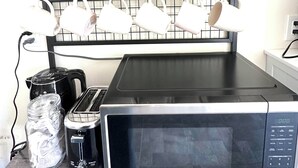 Eine Küchenarbeitsplatte mit einer Mikrowelle, einem Toaster und einem Glas mit zerknülltem Papier. Darüber befindet sich ein Regal mit einer Pflanze, einer Stretch-Tite-Box und einem Schild mit der Aufschrift 'Bitte alles ausschalten, bevor Sie gehen.'