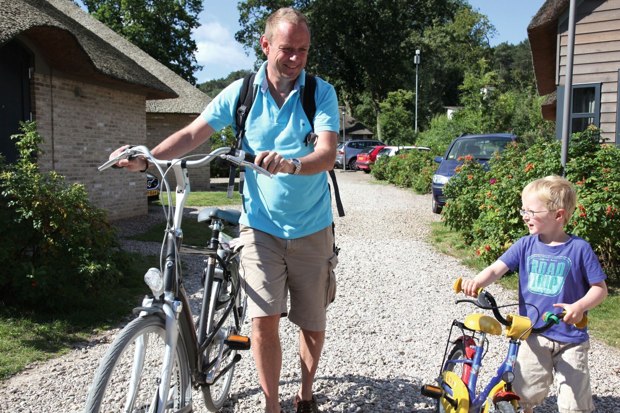 Un homme qui pousse un vélo et un enfant qui tient un vélo, tous deux sur un chemin de gravier.