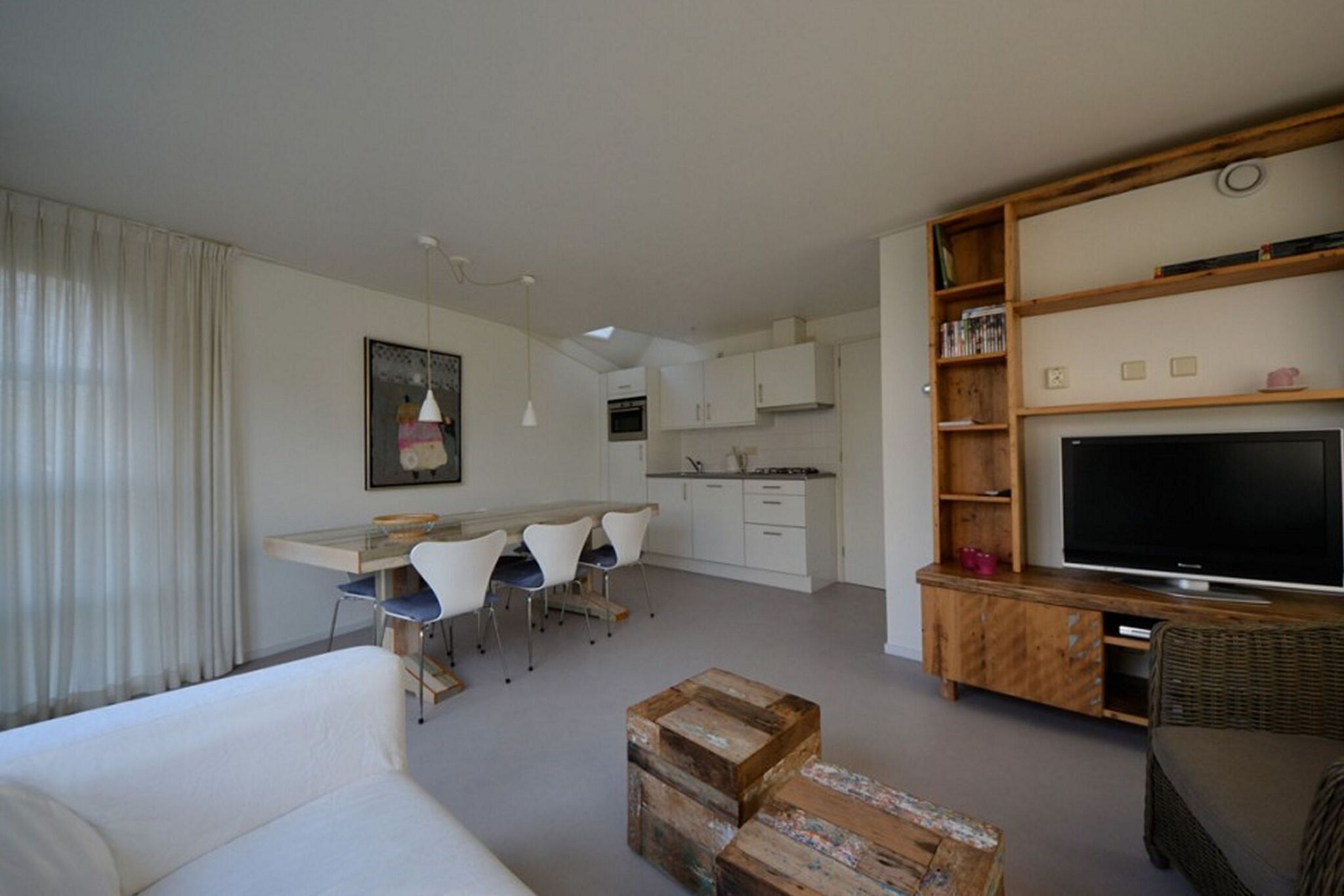 Una sala de estar moderna con un sofá, un comedor con sillas, una cocina con armarios y un televisor sobre un mueble de madera.
