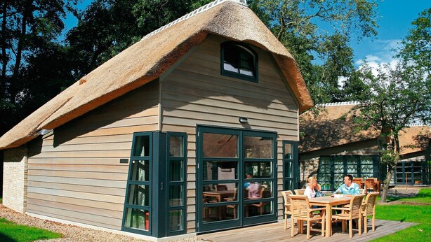 Een rieten huis met een houten terras en een eethoek.