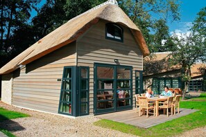 Une petite maison au toit de chaume, dotée d’une terrasse en bois et d’un coin repas.