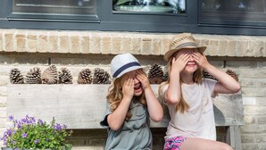 Twee kinderen zitten op een bank met dennenappels en een bloempot met de tekst '1928' voor een metselwerk schoorsteen.