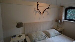 Een slaapkamer met een bed, twee nachtkastjes, een lamp op elk kastje en een aan de muur bevestigde decoratie van een hertengewei.