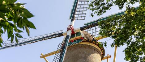 A traditional windmill with a brick base and a decorative top, surrounded by lush green foliage.