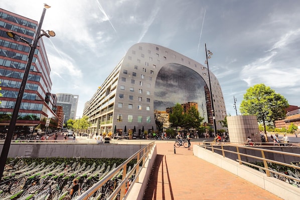 A modern building with a large arch entrance, surrounded by a plaza with bicycles and pedestrians.