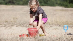 A child playing in a sandy area with a red bucket.