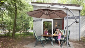 An outdoor patio with a table and chairs, a large umbrella, and a brick wall. - Pet-Friendly Retreat (Kootwijk)