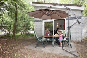Un patio al aire libre con una mesa, sillas, un paraguas grande y un muro de ladrillo.
