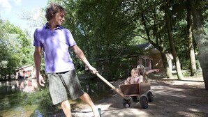 A person pushing a wheelbarrow with a child in it.