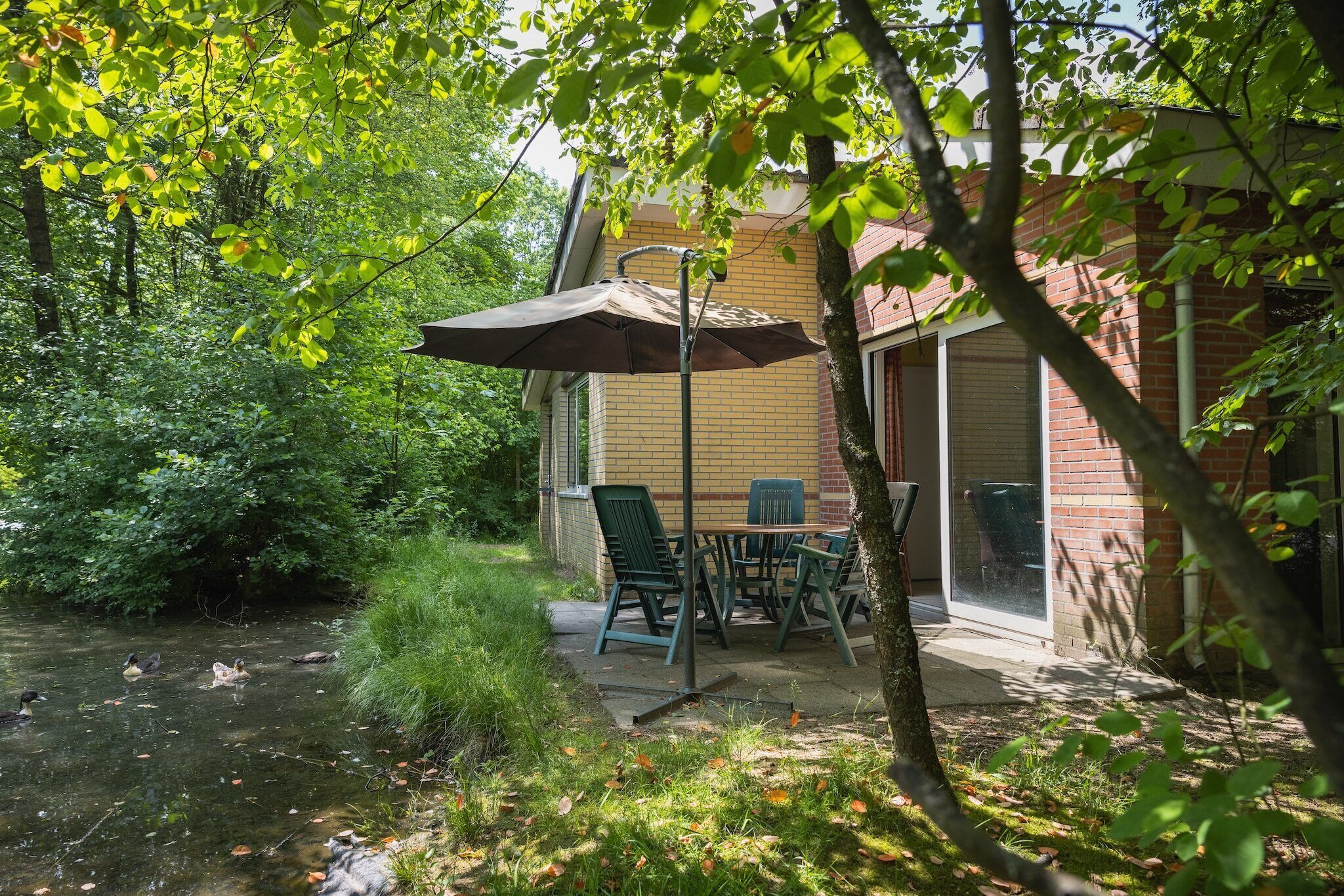 A patio with a table and chairs, a covered umbrella, and a view of a river with ducks.