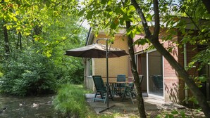 A patio with a table and chairs, a covered umbrella, and a view of a river with ducks.