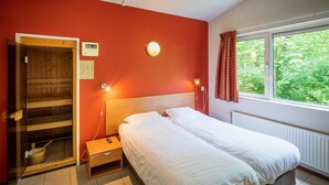A room with a bed, a sauna, a window with a view of greenery, and a thermostat on the wall.