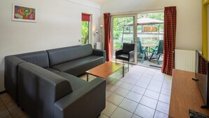 A living room with a sofa, a coffee table, and a TV. There is a sliding glass door leading to an outdoor area with chairs and a table.
