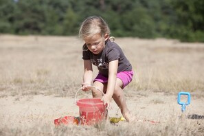 Un niño jugando en una zona arenosa con un cubo rojo.
