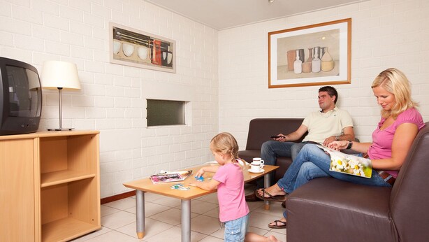 A living room with a television, a coffee table, and a child playing. - Bungalow in Netherlands with Sauna & Privacy (Kootwijk)