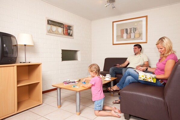 A living room with a television, a coffee table, and a child playing. - Bungalow in Netherlands with Sauna & Privacy (Kootwijk)