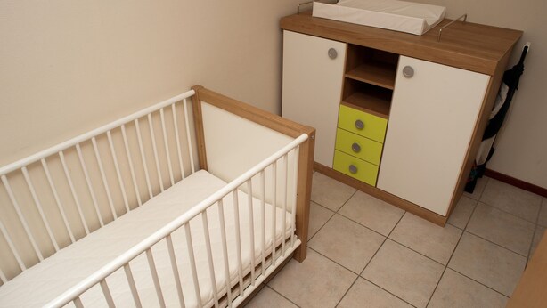A baby crib with a wooden side table and a cabinet with drawers.