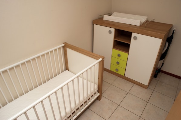 A baby crib with a wooden side table and a cabinet with drawers.