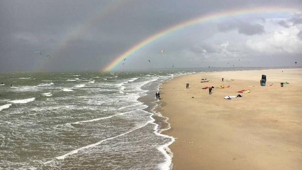 Une plage avec un arc-en-ciel, des vagues et des gens.