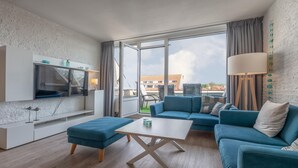 Un salon moderne avec un canapé, un pouf et un téléviseur fixés sur un mur blanc.