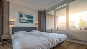 Une chambre moderne avec un grand lit, une vue sur l’extérieur et un tableau représentant une mouette accroché au mur.