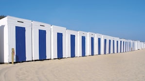 Une rangée de petits bâtiments modulaires blancs, avec des portes bleues, sur une plage de sable.
