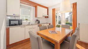 A compact kitchen with a microwave, stove, and cabinets. There is a dining table with chairs and a hanging light fixture. - Country House in AquaStaete with Veranda (Bruinisse)