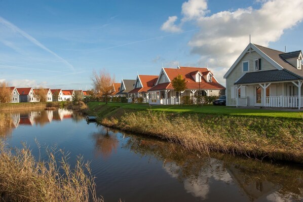 A row of white houses with red roofs and a calm water body in the foreground.