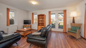 A living room with a leather sofa, a wooden coffee table, a television, a bookshelf, and a wicker chair. - Country House in AquaStaete with Veranda (Bruinisse)