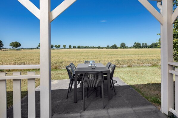 A covered outdoor dining area with a table and chairs, overlooking a field.