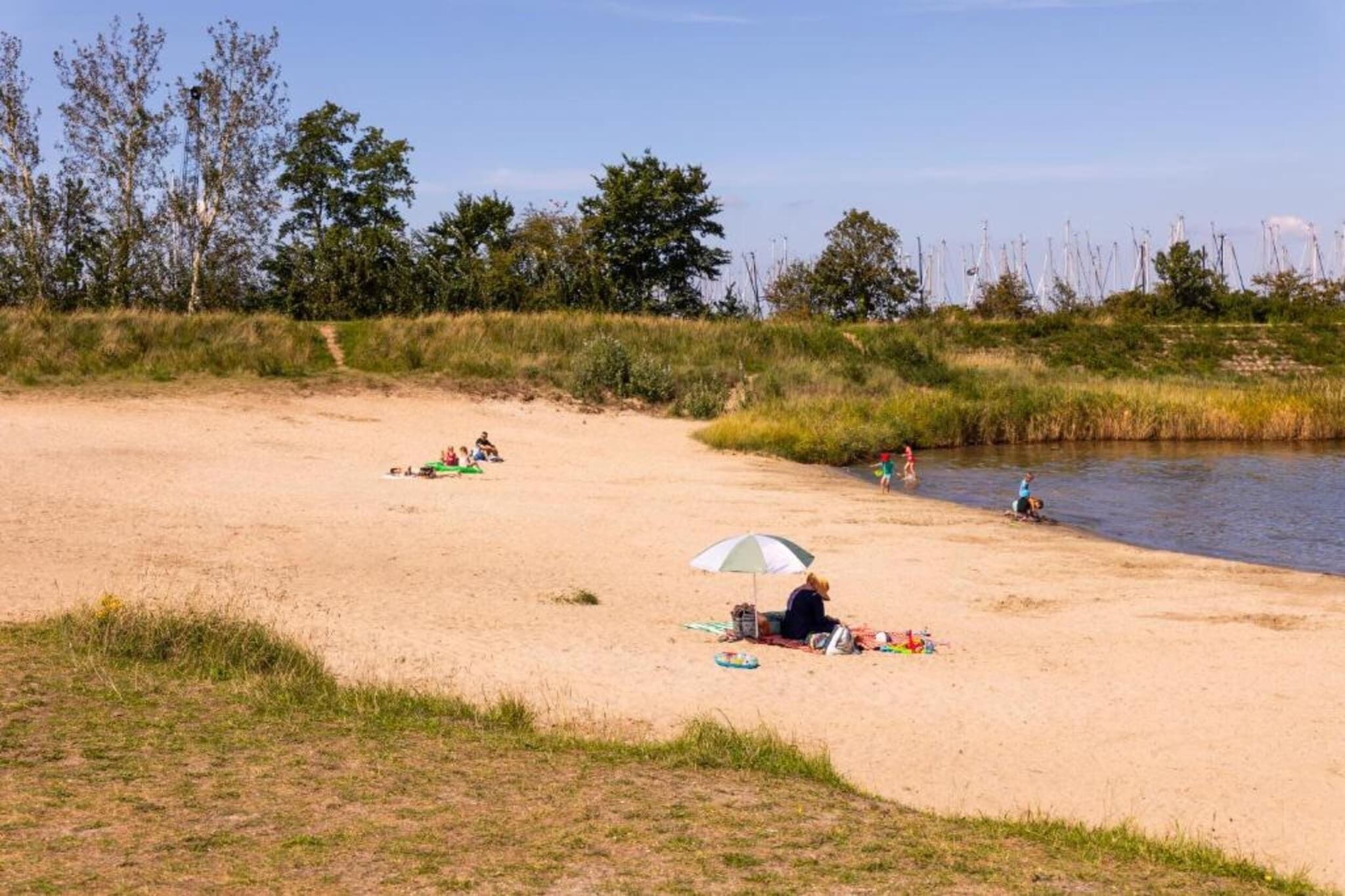 Ein Sandstrand mit entspannten Menschen, einem Zelt und ruhigem Wasser.