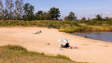 Ein Sandstrand mit entspannten Menschen, einem Zelt und ruhigem Wasser.