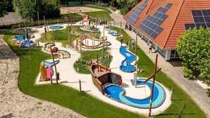 A playground with various play structures, a small pool, and a building with solar panels. - Villa in Aquadelta with Sauna & Jacuzzi (Bruinisse)
