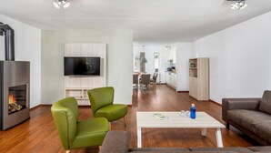 A modern living room with a fireplace, green and brown sofas, a TV, and a dining area in the background. - Villa in Aquadelta with Sauna & Jacuzzi (Bruinisse)