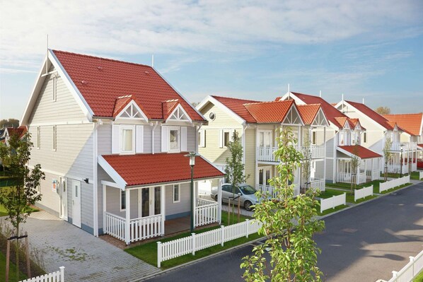 A row of white houses with red roofs and white railings, arranged in a residential street.