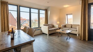 A spacious living room with a wooden dining table, two sofas, and large windows offering a view of the cityscape. - Modern Domburg Apartment (Domburg)