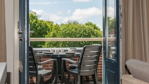 An open sliding glass door leading to a balcony with a table and chairs, a view of greenery, and a clear sky. - Modern Domburg Apartment (Domburg)
