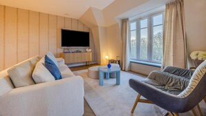 A modern living room with a flat-screen TV, a sofa, a chair, a small table, and a window with curtains. - Apartment in Domburg near the Beach (Domburg)