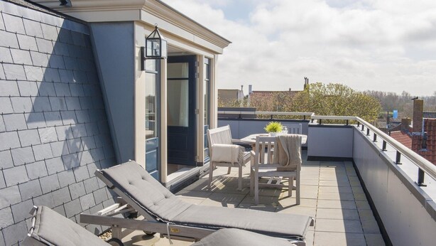 A rooftop terrace with two lounge chairs, a table with chairs, a potted plant, and a door leading to an interior space. - Apartment in Domburg near the Beach (Domburg)