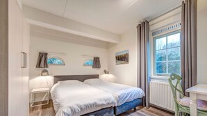 A bedroom with two beds, a window with curtains, a radiator, and a chair. - Villa in Domburg near North Sea Beach (Domburg)
